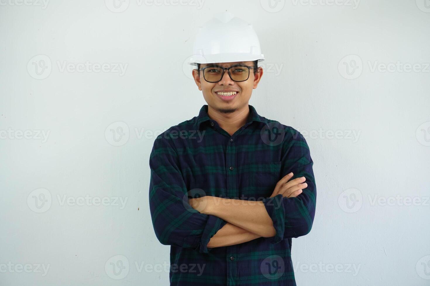 joven asiático hombre es ingeniero vistiendo casco en pie con cruzado brazos y sonriente con seguro, arquitecto o contratista, trabajador o mano de obra, industrial concepto. foto