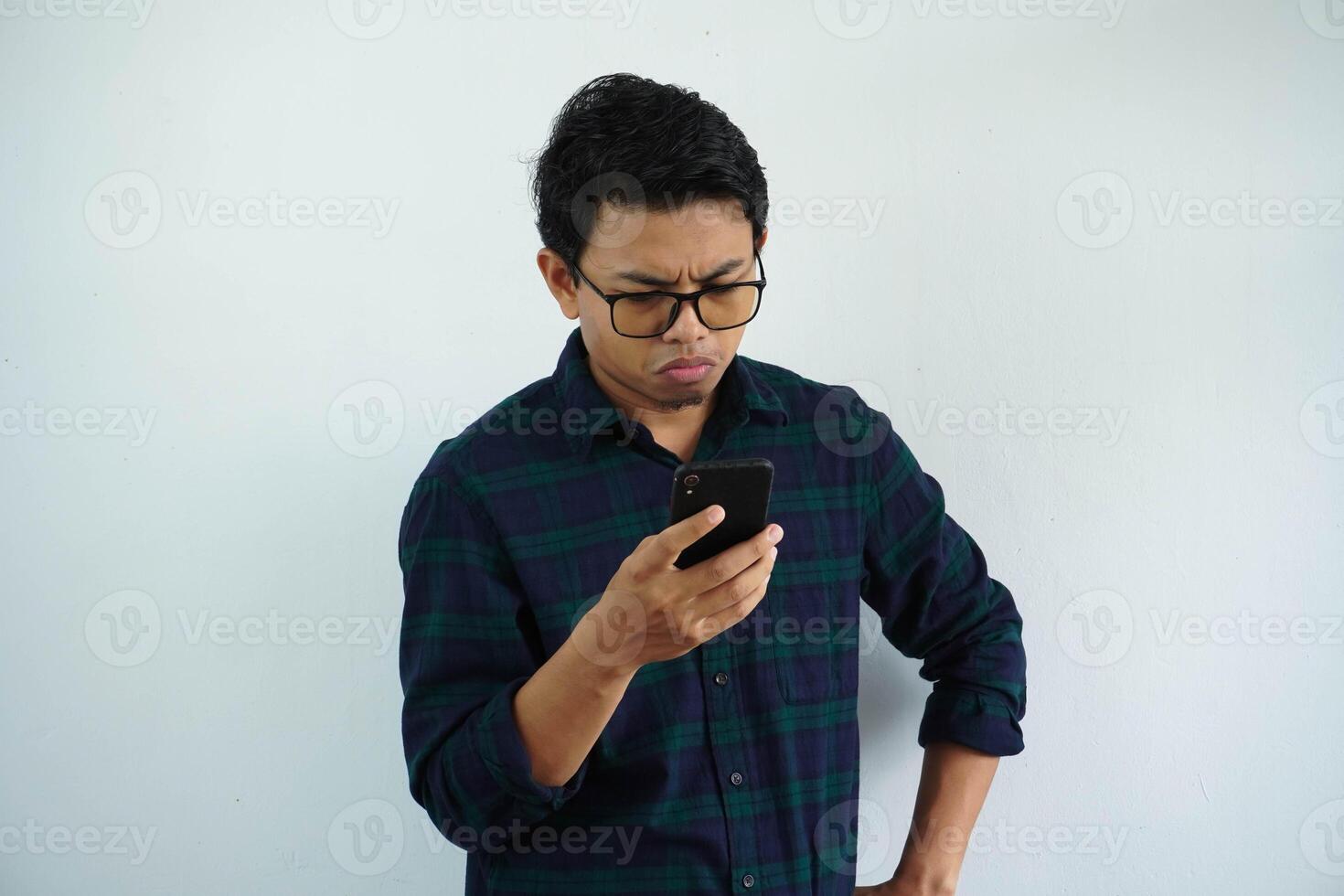 serious young asian man looking this phone with hands on waist isolated on white background photo