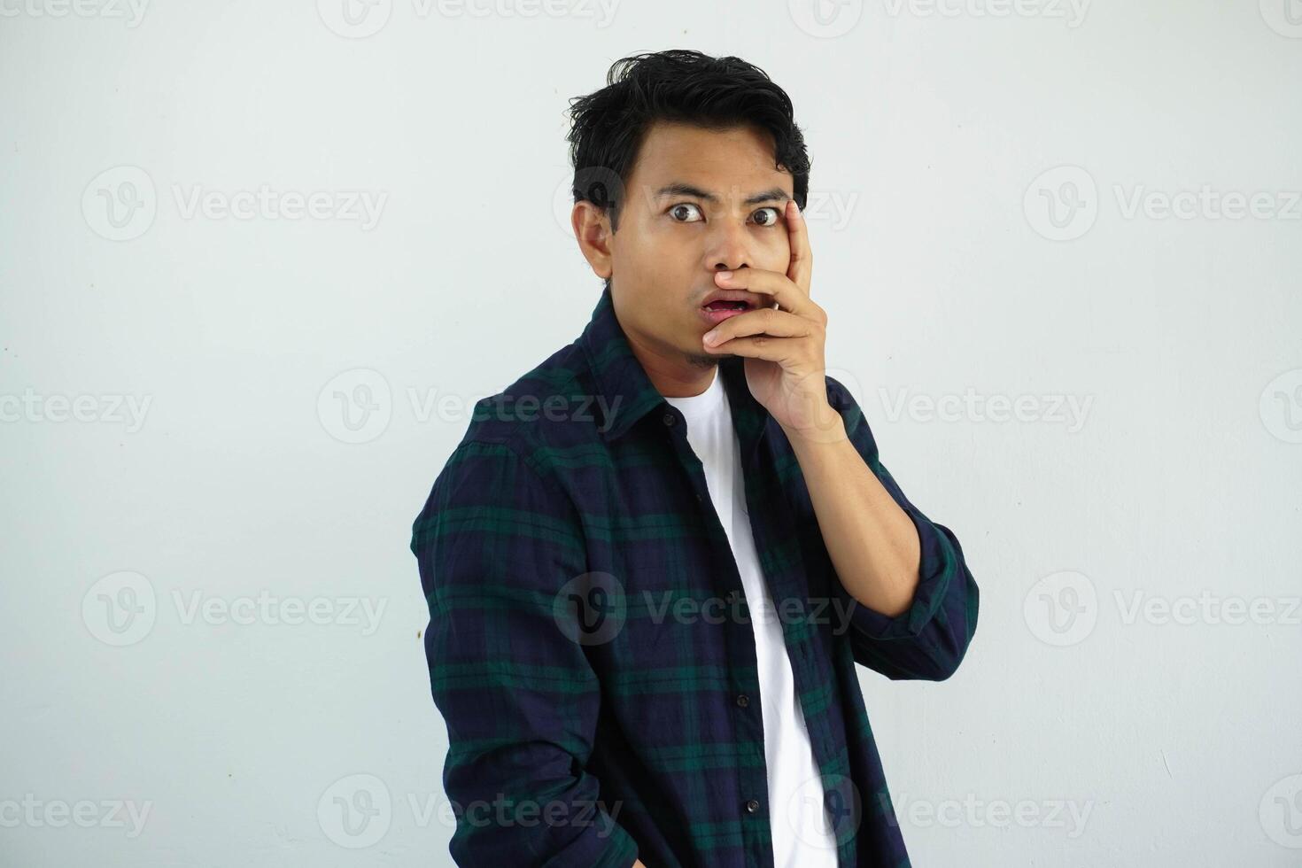 Asian young man showing shocked facial expression with hands partially covering face isolated on white background. photo