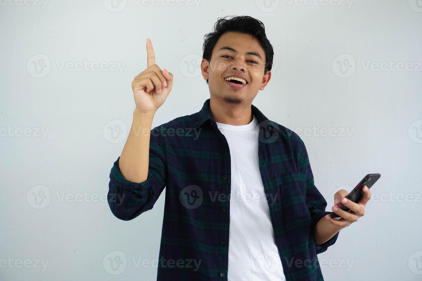 young asian man showing happy expression with finger pointing up when holding mobile phone isolated on white background photo