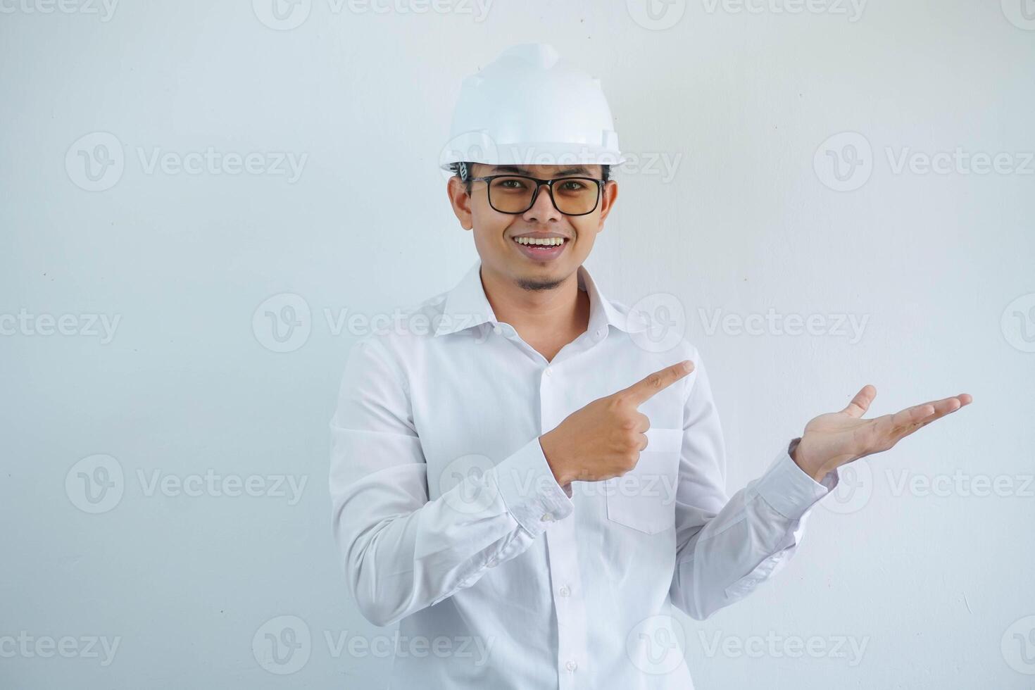 joven asiático arquitecto hombre vistiendo blanco difícil sombrero la seguridad casco mirando cámara con dedo señalando a su abierto mano palma aislado en blanco antecedentes foto