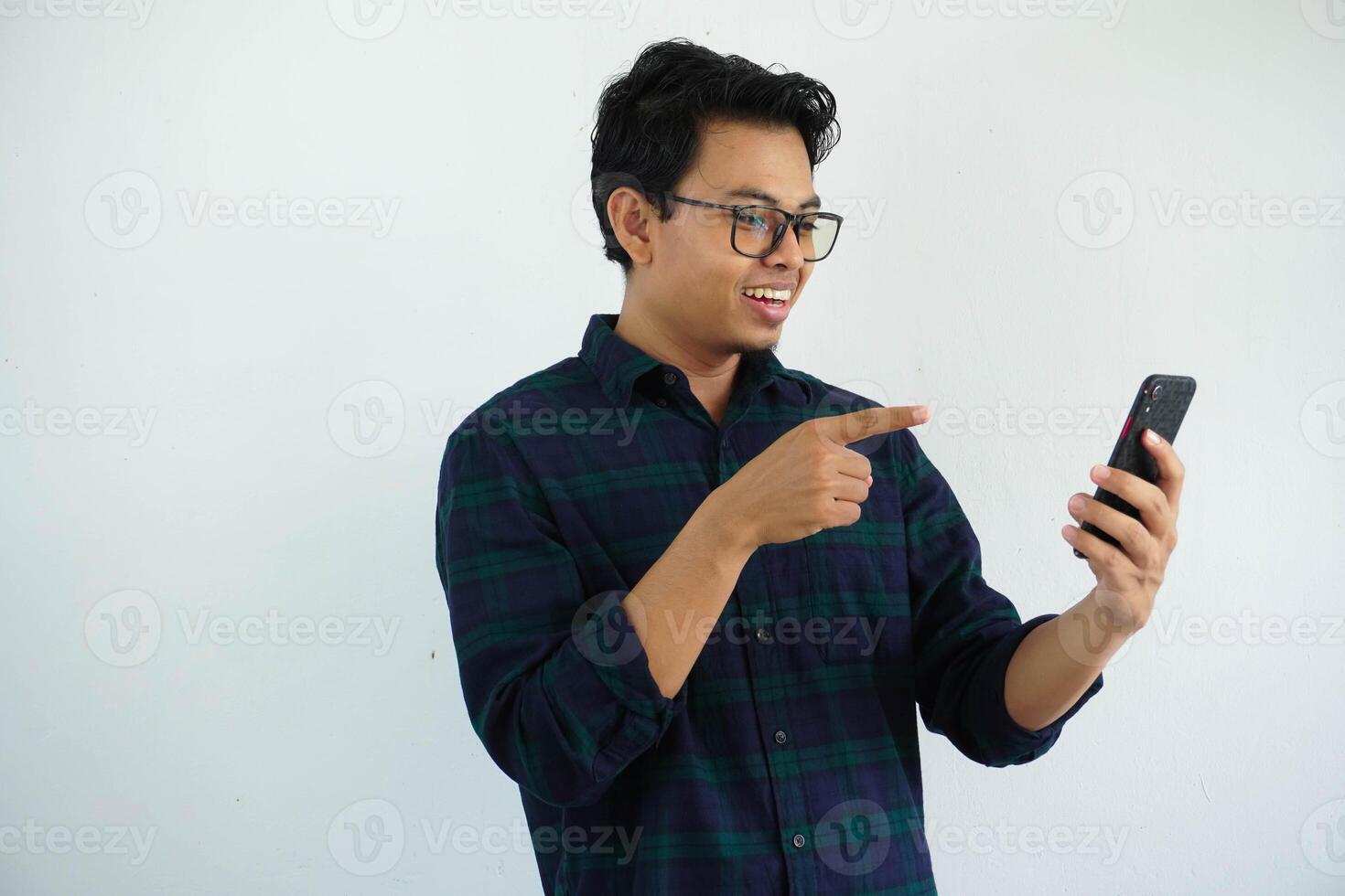 smiling young asian man when looking to his mobile phone and point with a finger isolated on white background photo