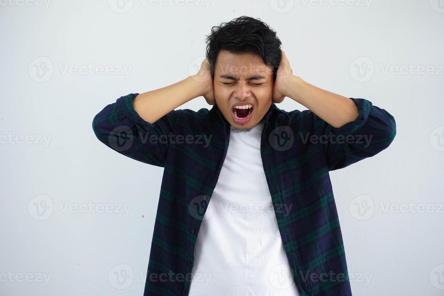 young asian man showing angry face expression while close his ears with both hand isolated on white background photo