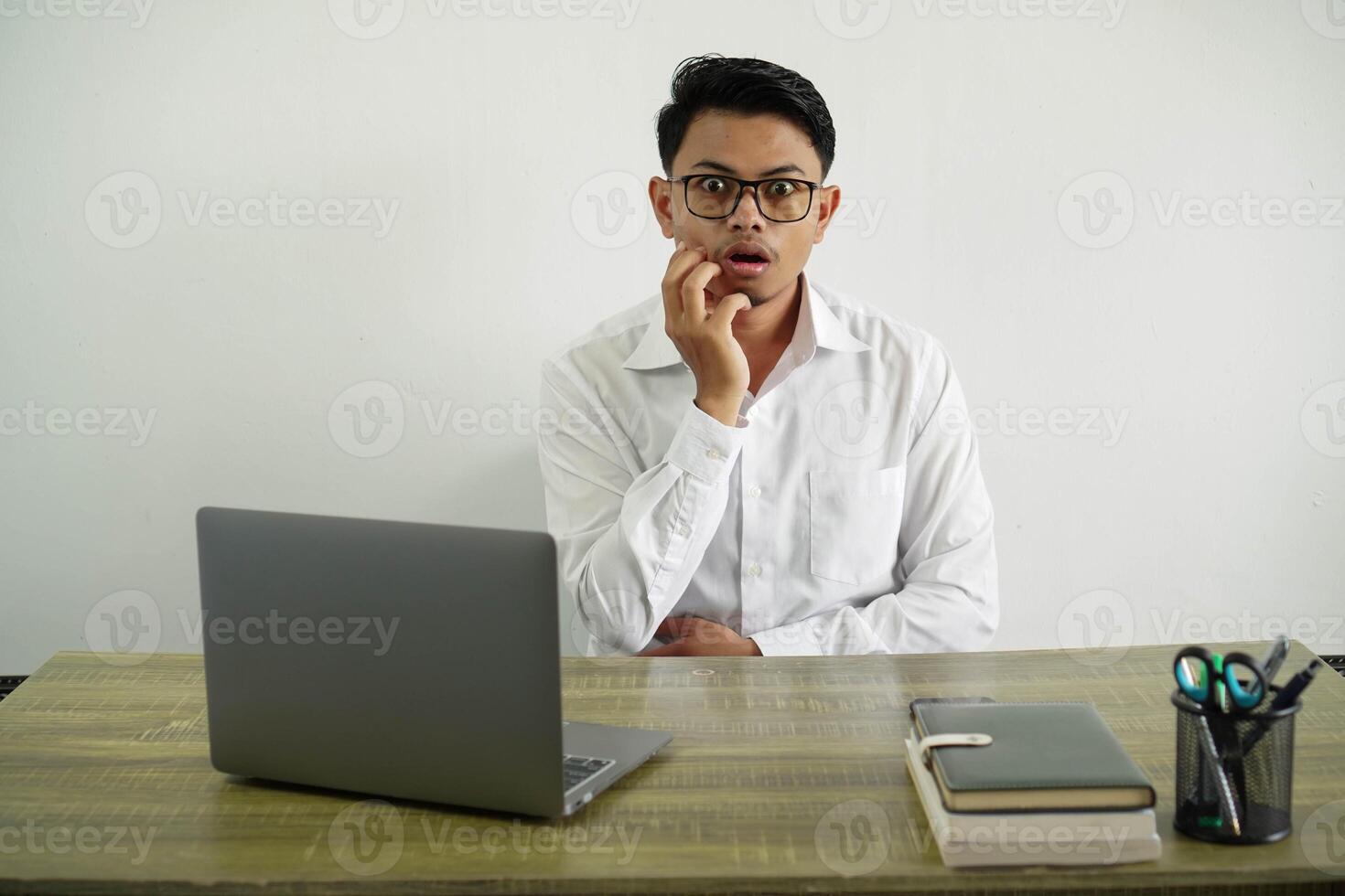 young asian businessman in a workplace surprised and shocked while looking right, wear white shirt with glasses isolated photo