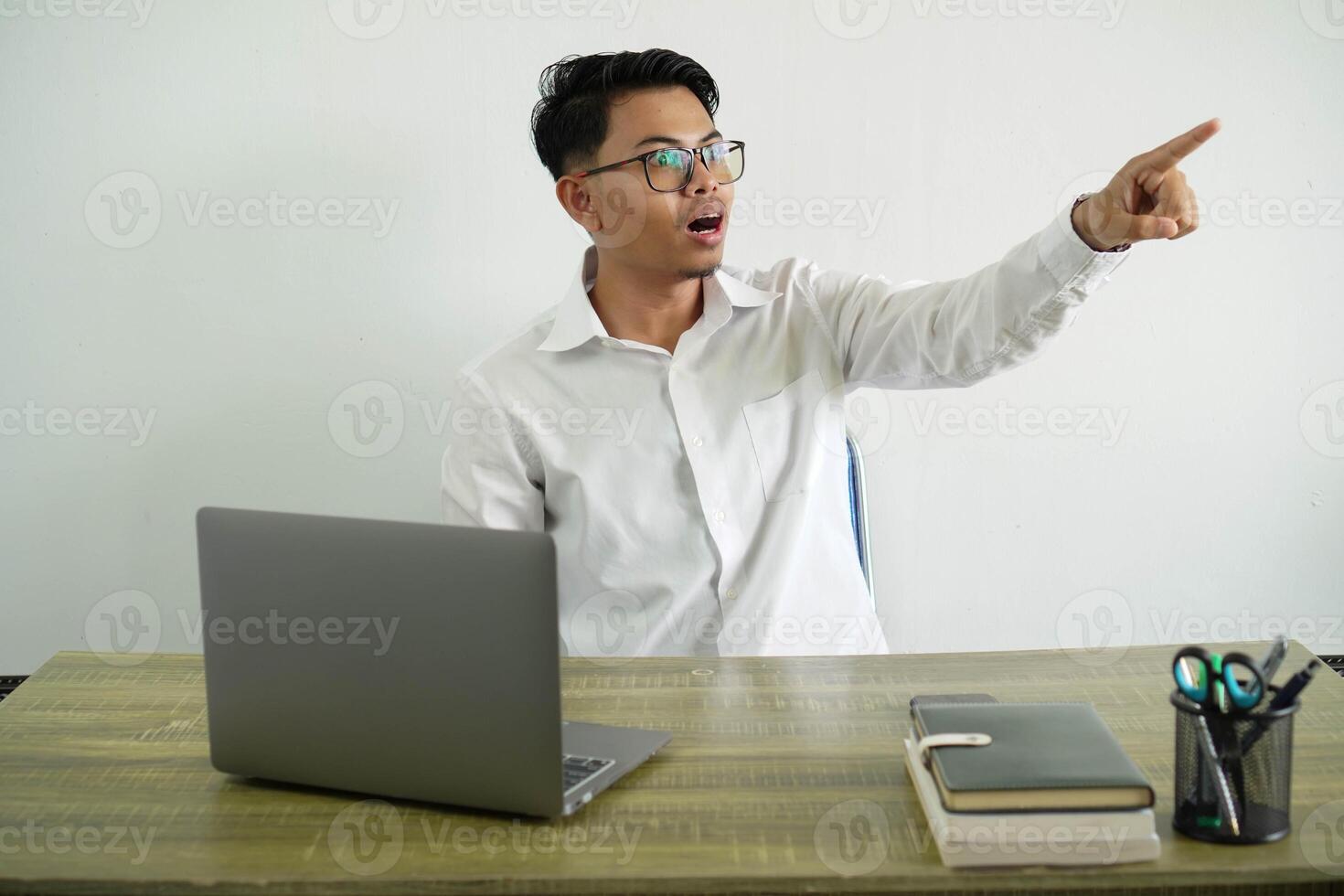 young asian businessman in a workplace pointing away with fingers, wear white shirt with glasses isolated photo