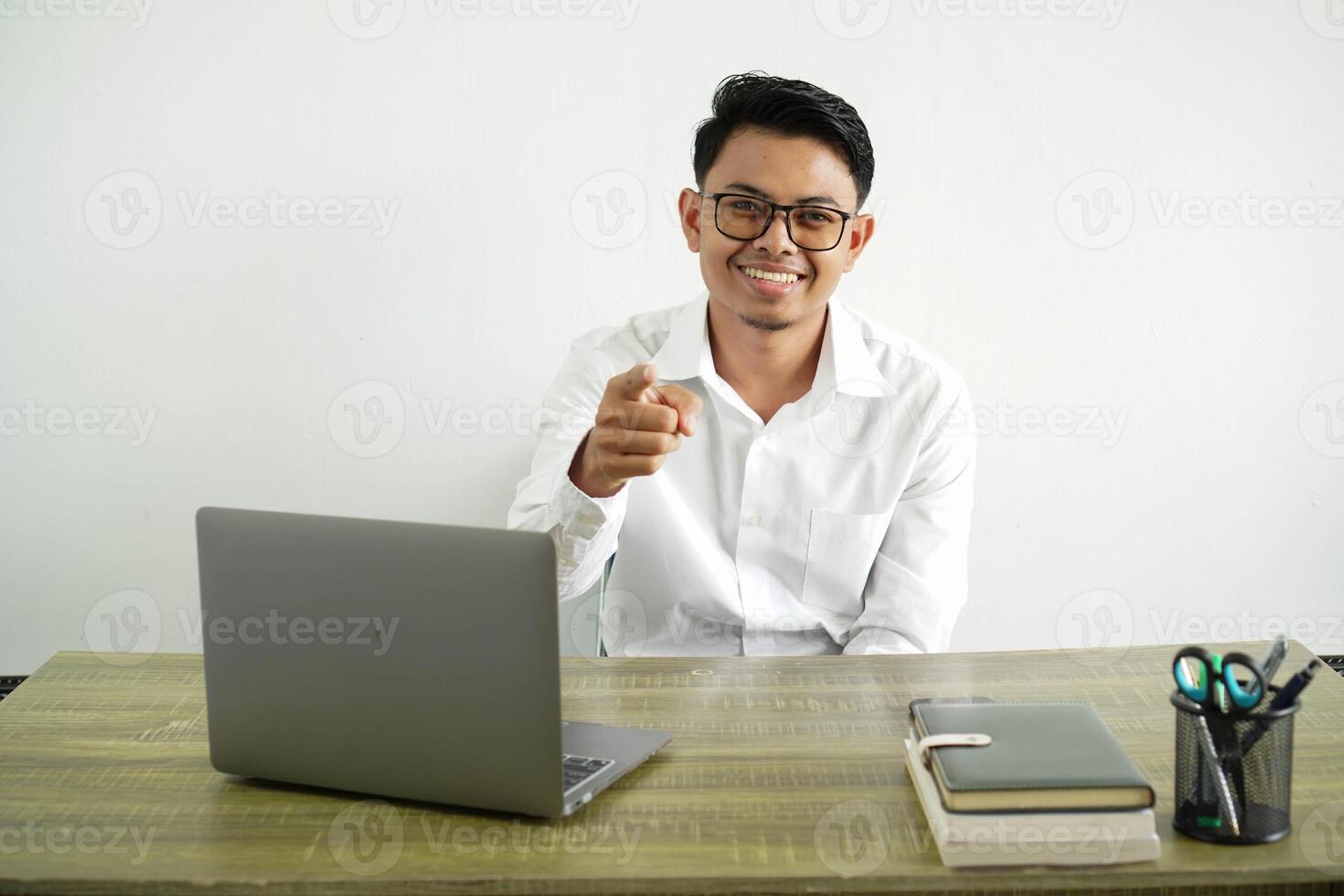 young asian businessman in a workplace surprised and pointing front, wear white shirt with glasses isolated photo