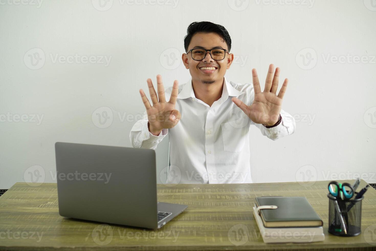 smiling young asian businessman in a workplace counting nine with fingers, wear white shirt with glasses isolated photo