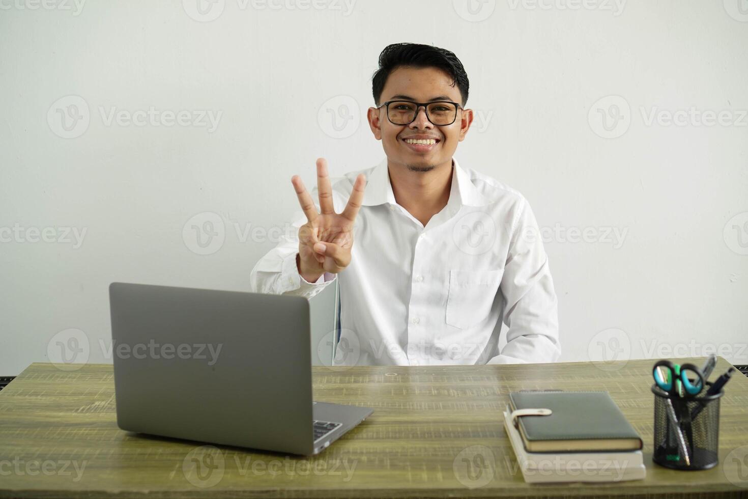smiling young asian businessman in a workplace happy counting three with fingers, wear white shirt with glasses isolated photo