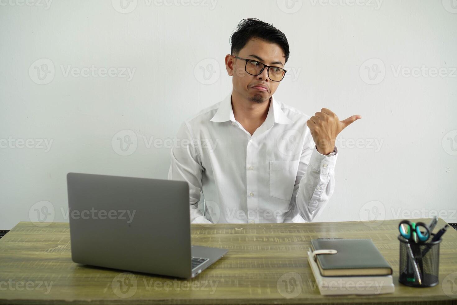 young asian businessman in a workplace unhappy and pointing to the side, wearing white shirt with glasses isolated photo