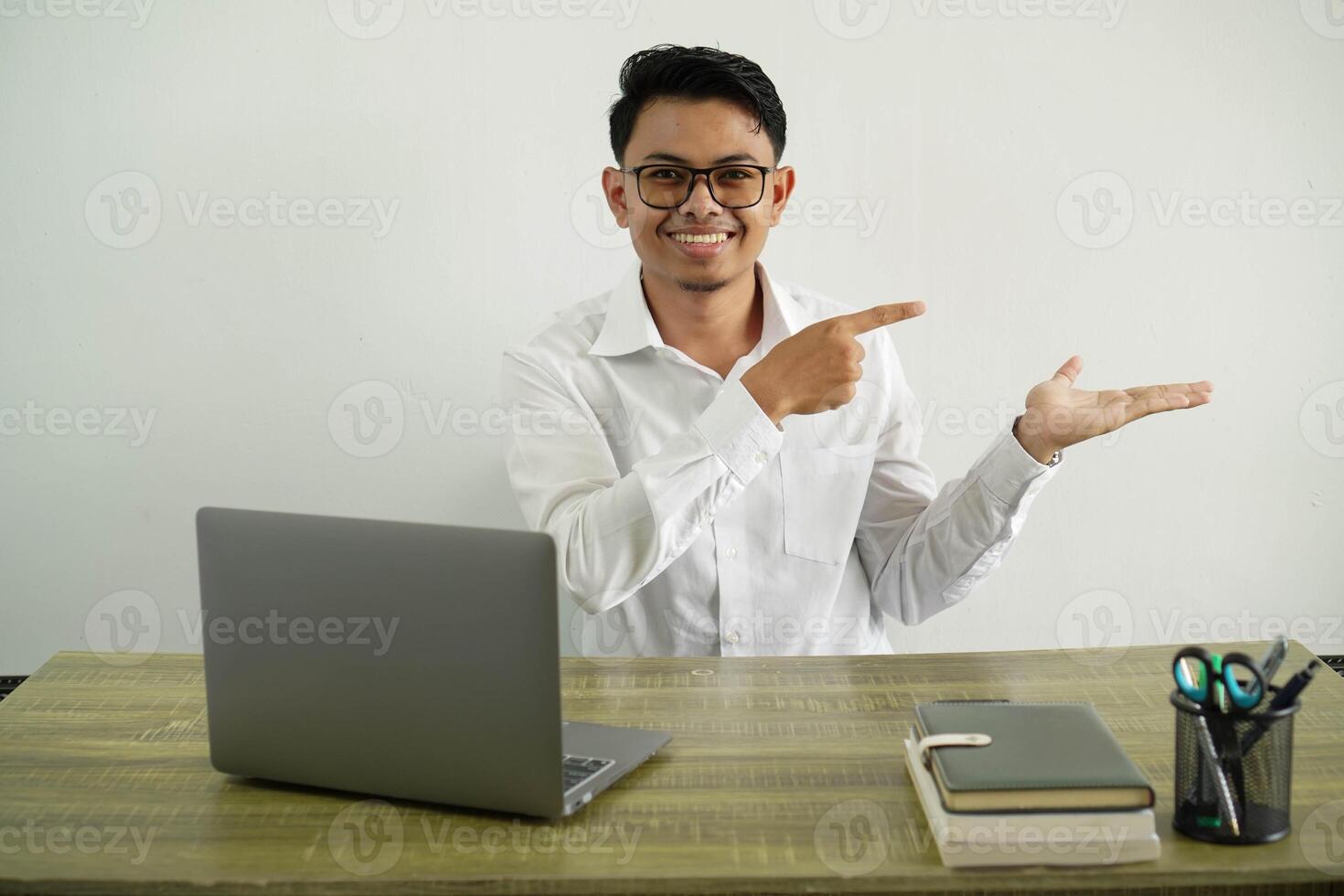 young asian businessman in a workplace holding copyspace imaginary on the palm to insert an ad, wearing white shirt with glasses isolated photo