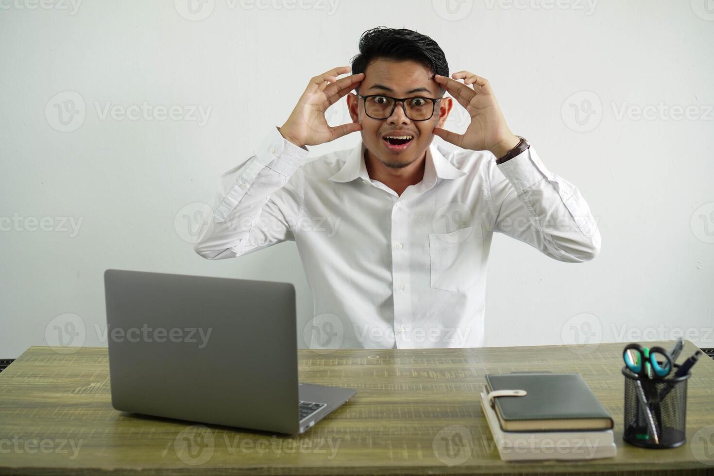 young asian businessman in a workplace with surprise expression, wear white shirt with glasses isolated photo