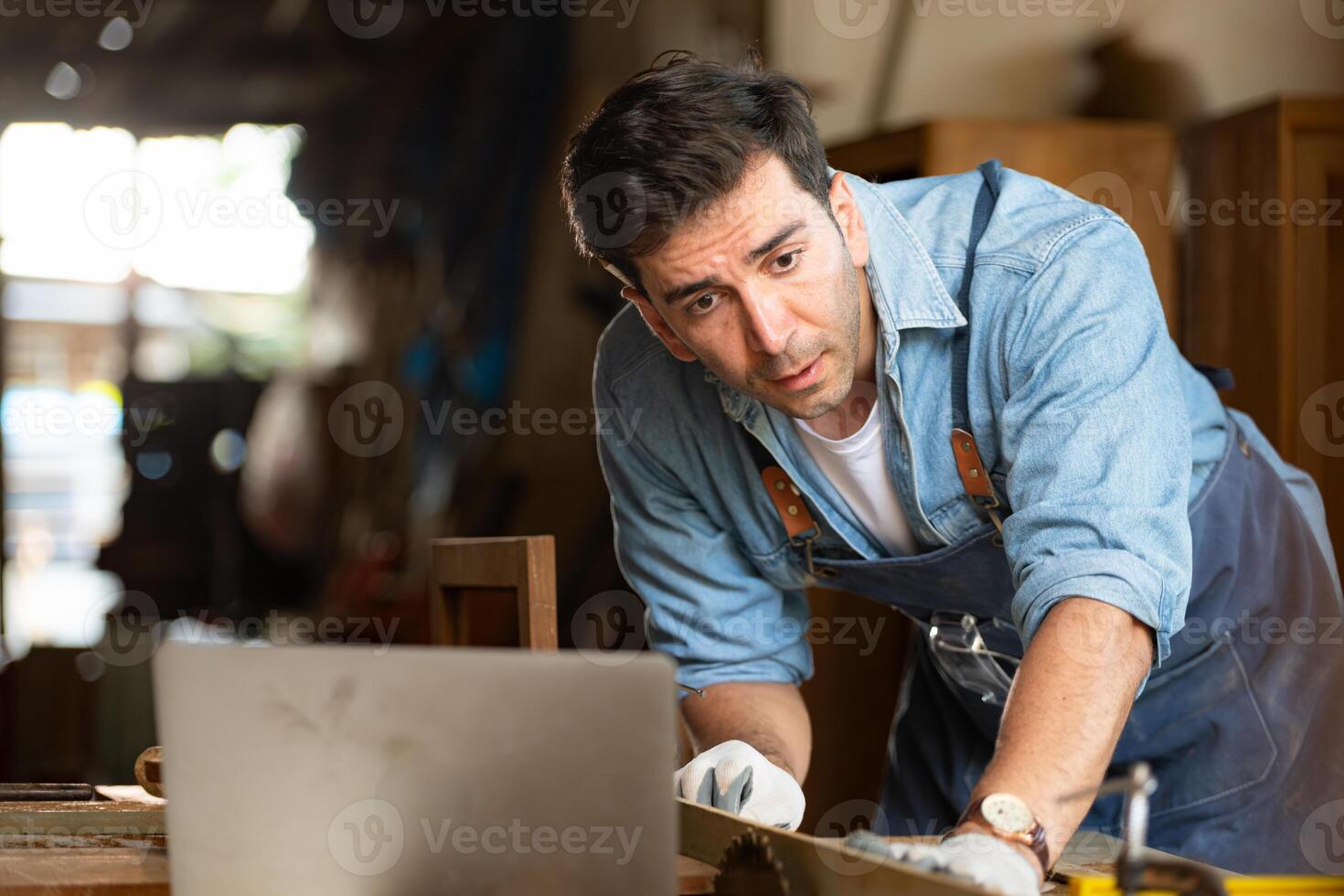 Carpenter working on laptop in his workshop at a woodworking factory photo