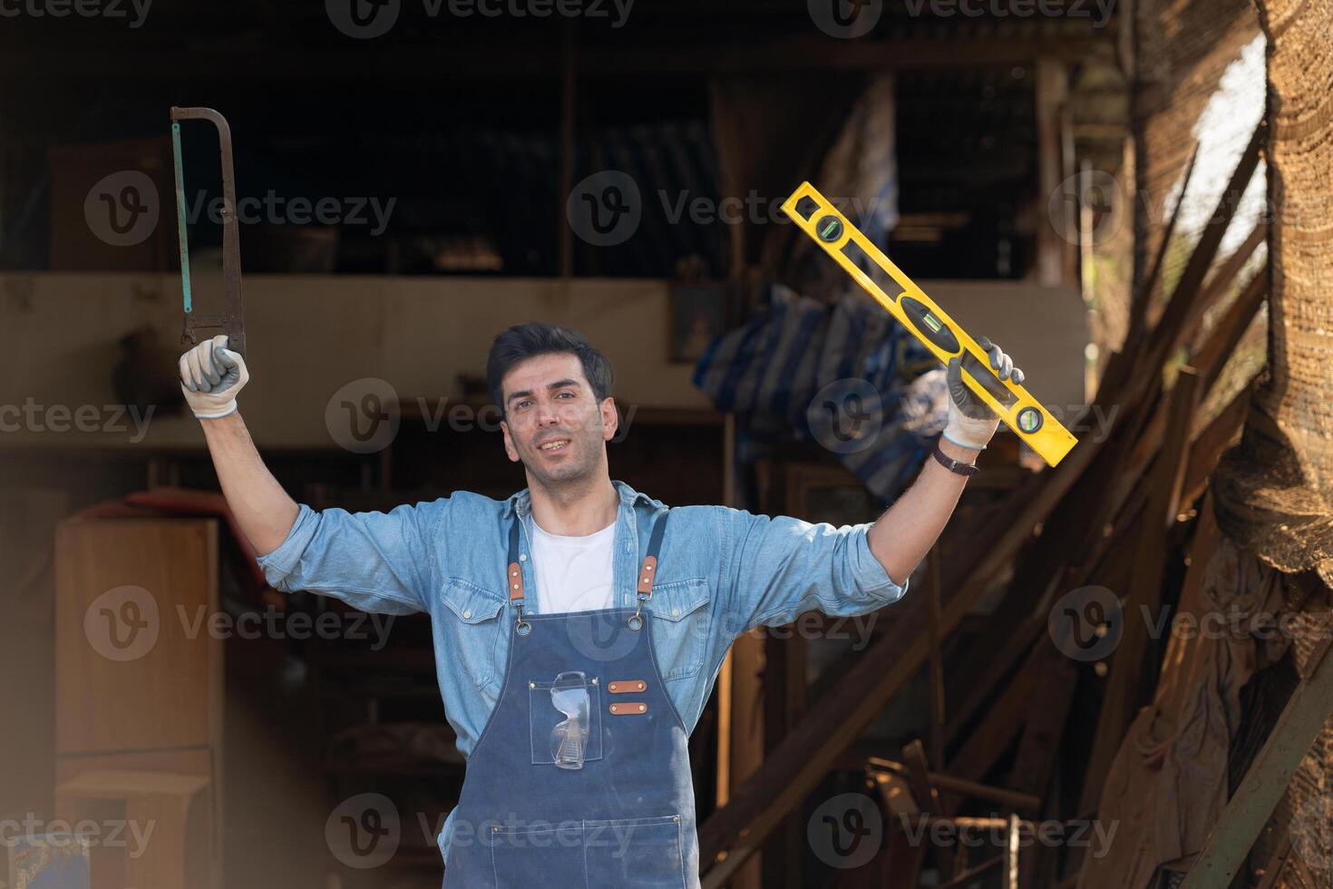 Portrait of a carpenter holding a spirit level and handsaw in his workshop. photo