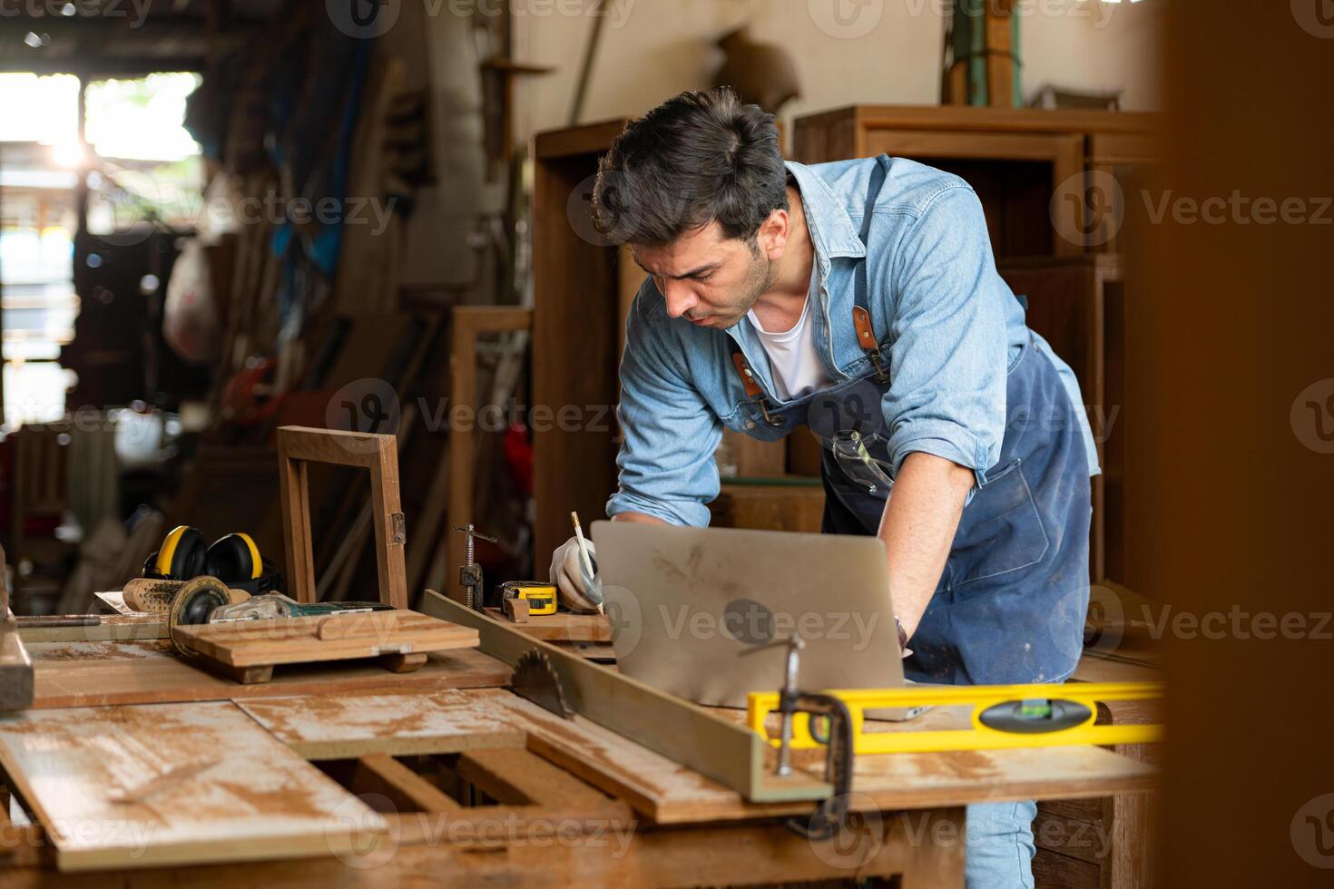 Carpenter working on laptop in his workshop at a woodworking factory photo