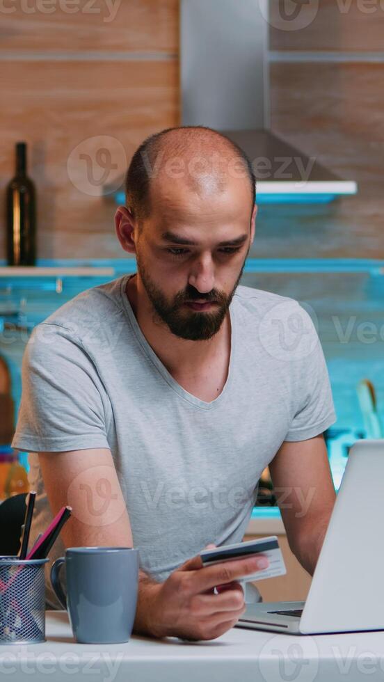 Freelancer making transaction from home using credit card sitting in the kitchen late at night. Freelancer shopping online from home with electronic paymant on digital notebook conected to internet photo