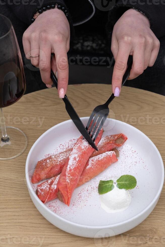 Plate with sweet pink pancakes and ice cream and female hands with cutlery angle view photo