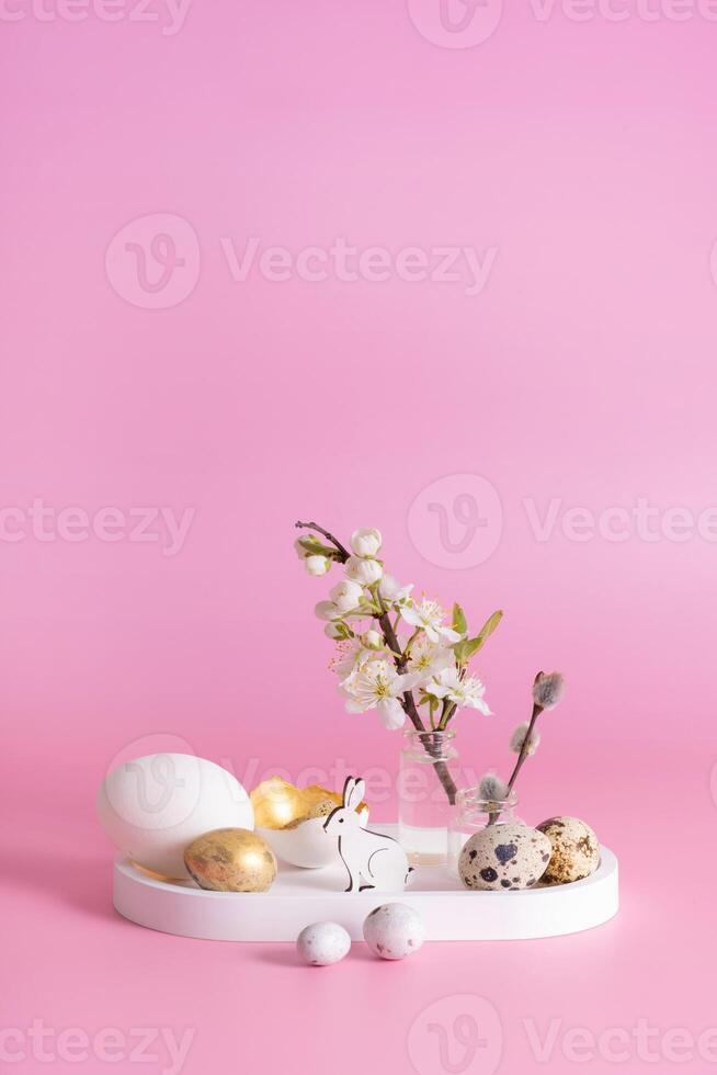 blanco conejo, florecer ramita y dorado Pascua de Resurrección huevos en un rosado antecedentes. Pascua de Resurrección todavía vida composición foto