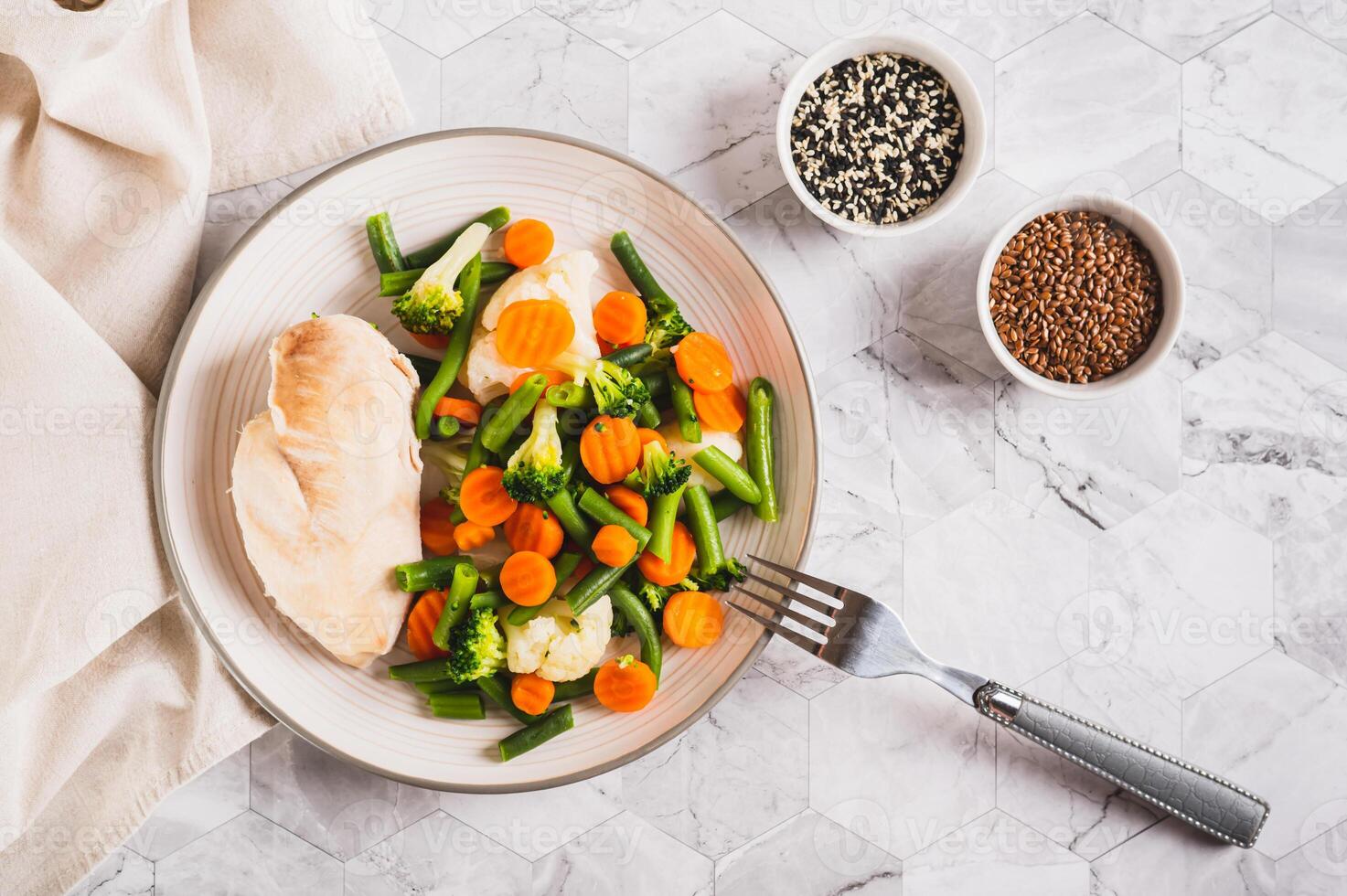 Mixed vegetables and steamed chicken breast on a plate on the table top view photo