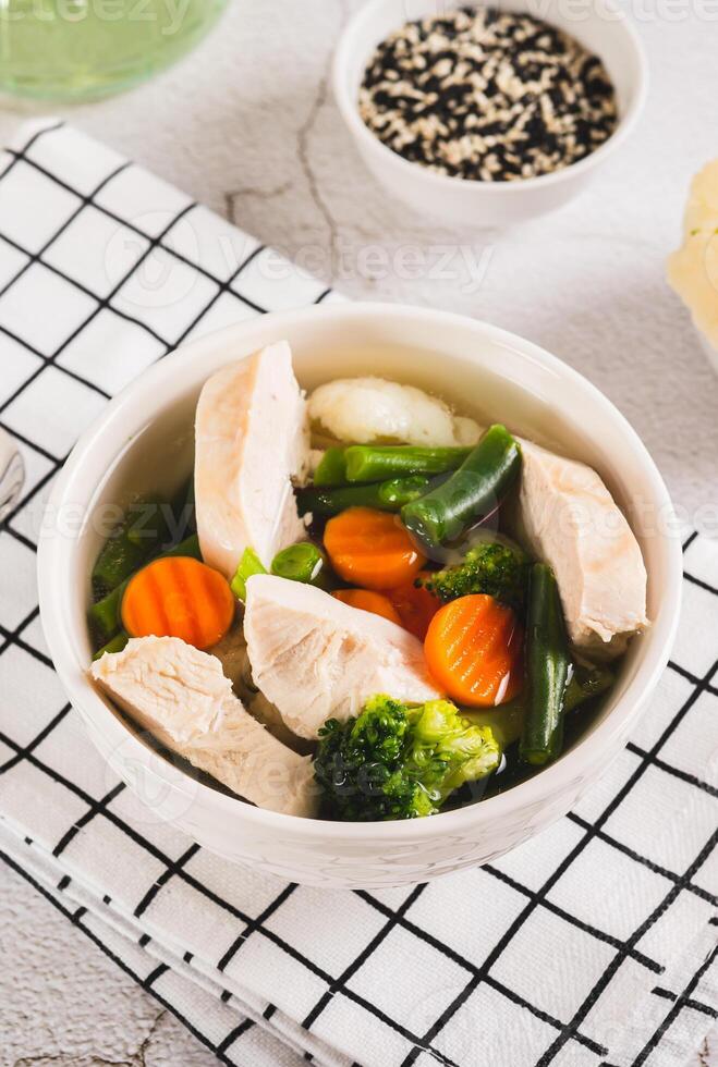 Diet soup with chicken fillet and boiled vegetables in a bowl on the table vertical view photo