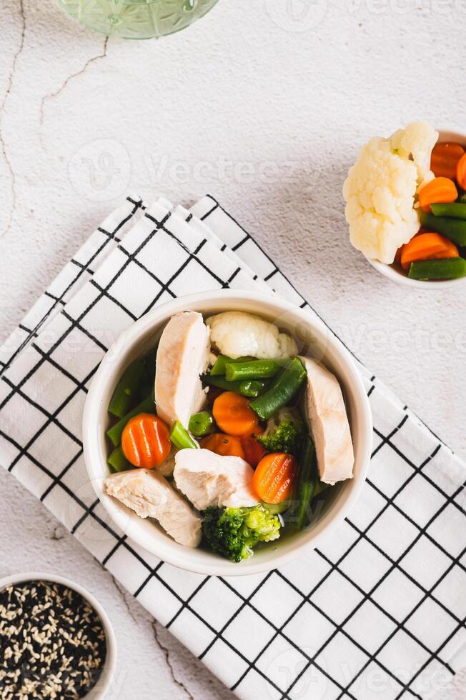 Diet soup with chicken fillet and boiled vegetables in a bowl on the table top and vertical view photo