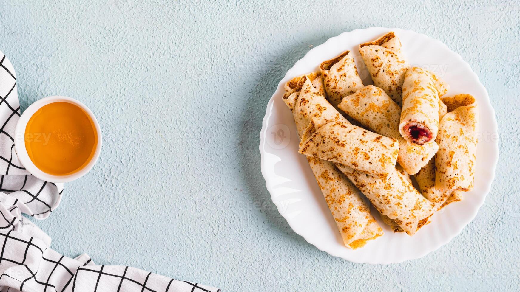 Thin pancakes rolled into rolls with berry jam on a plate on the table top view web banner photo