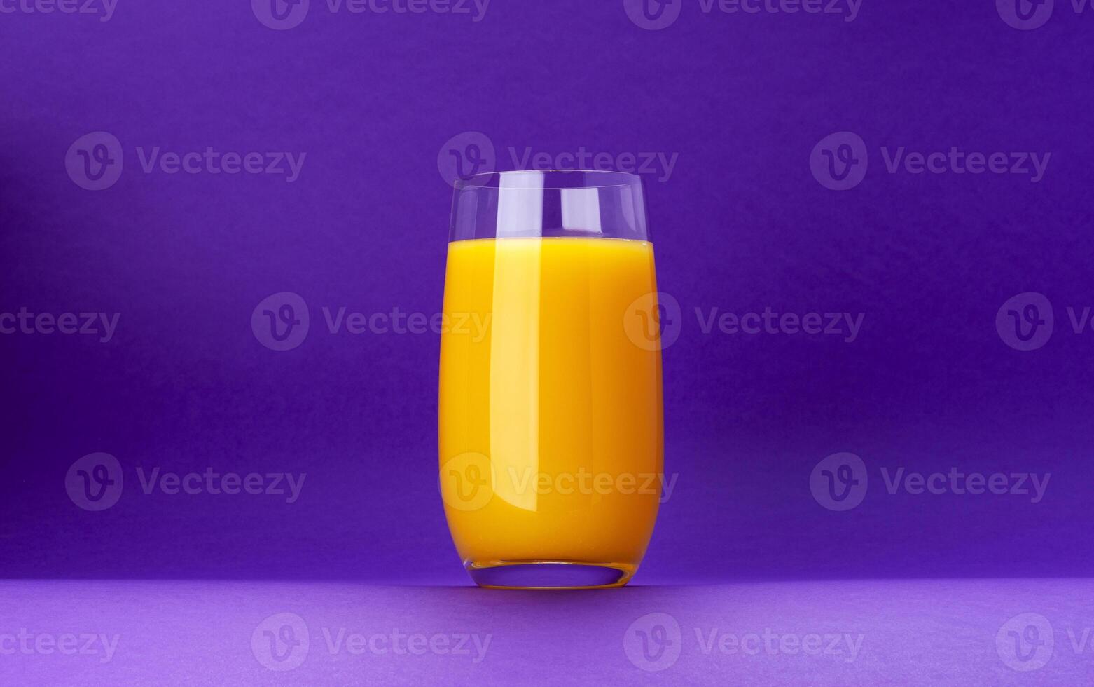 Glass of orange juice isolated on violet background with copy space photo