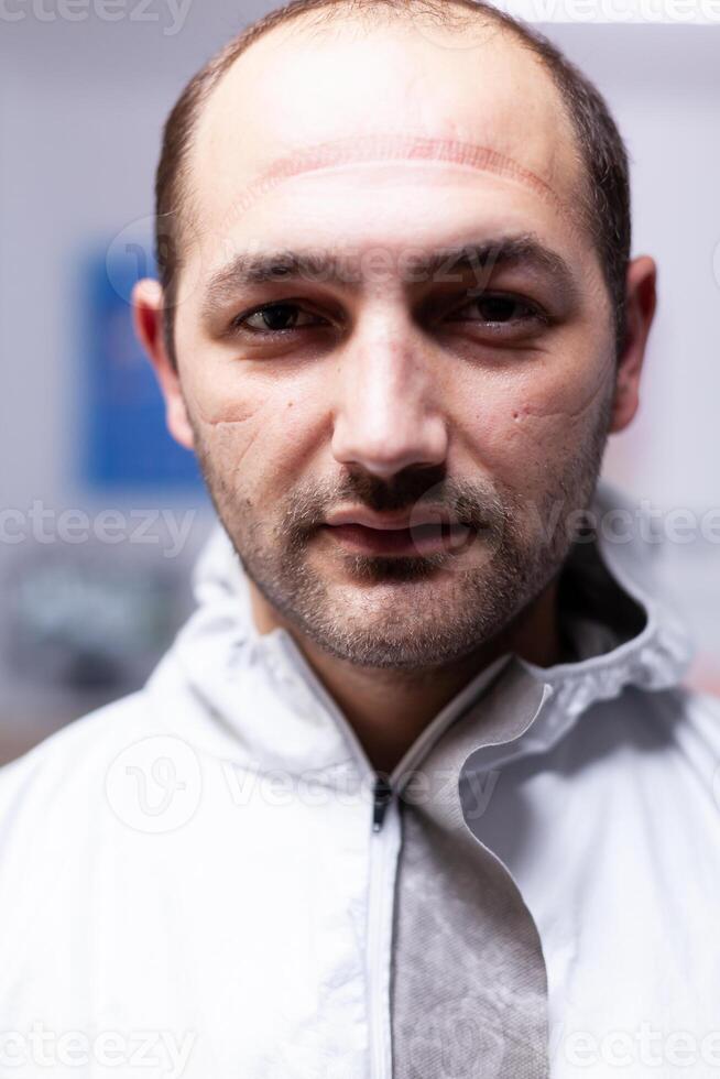 Close up of exhausted pediatric dentist man marks on face because of protection mask. Portrait of tired stomatologist wearing coronavirus ppe suit looking at camera. photo