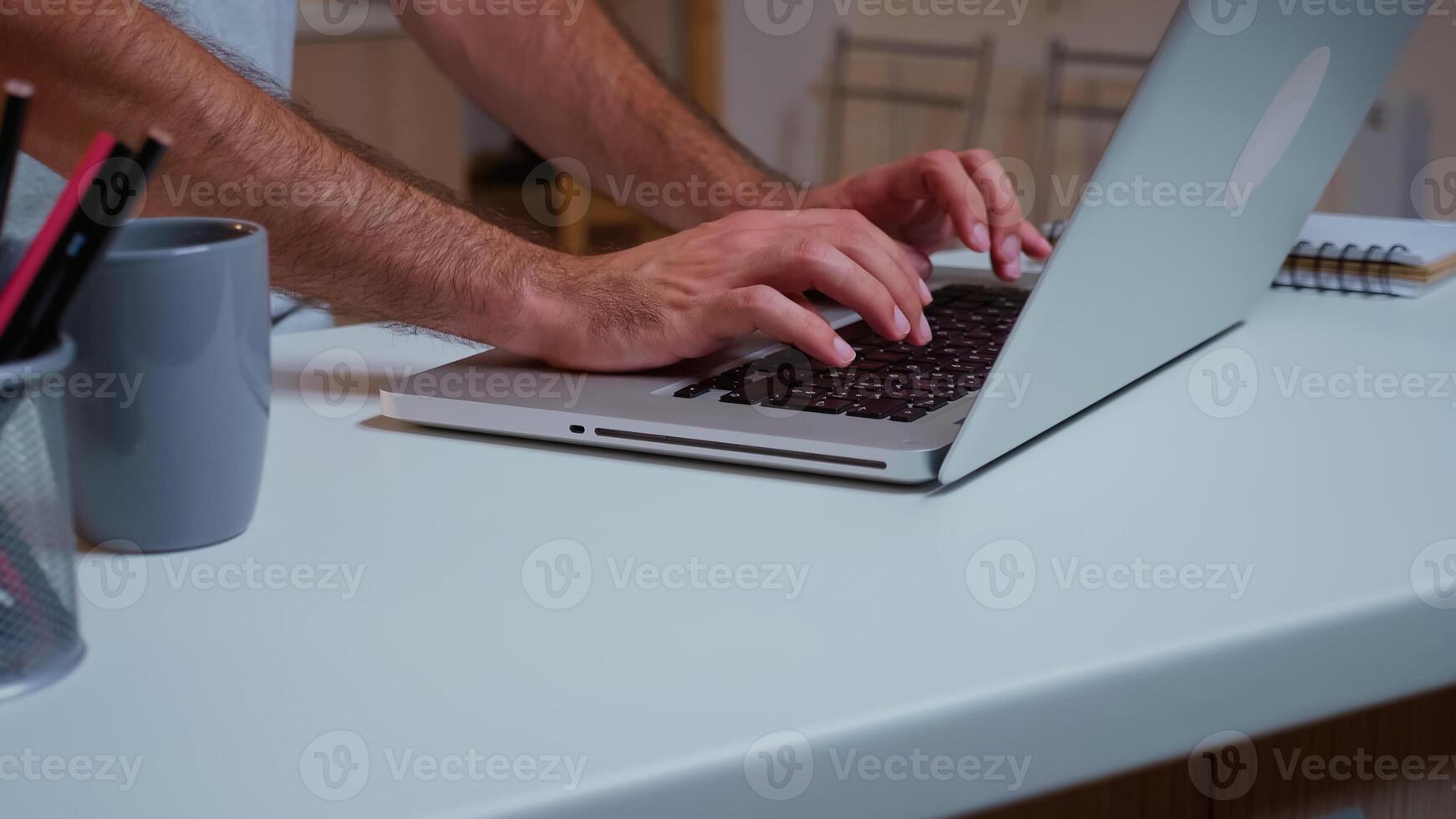 cerca arriba de del hombre manos mecanografía en ordenador portátil sentado en el cocina tarde a noche y laboral. ocupado empleado utilizando moderno tecnología red inalámbrico haciendo tiempo extraordinario para trabajo leyendo escribiendo, buscando foto