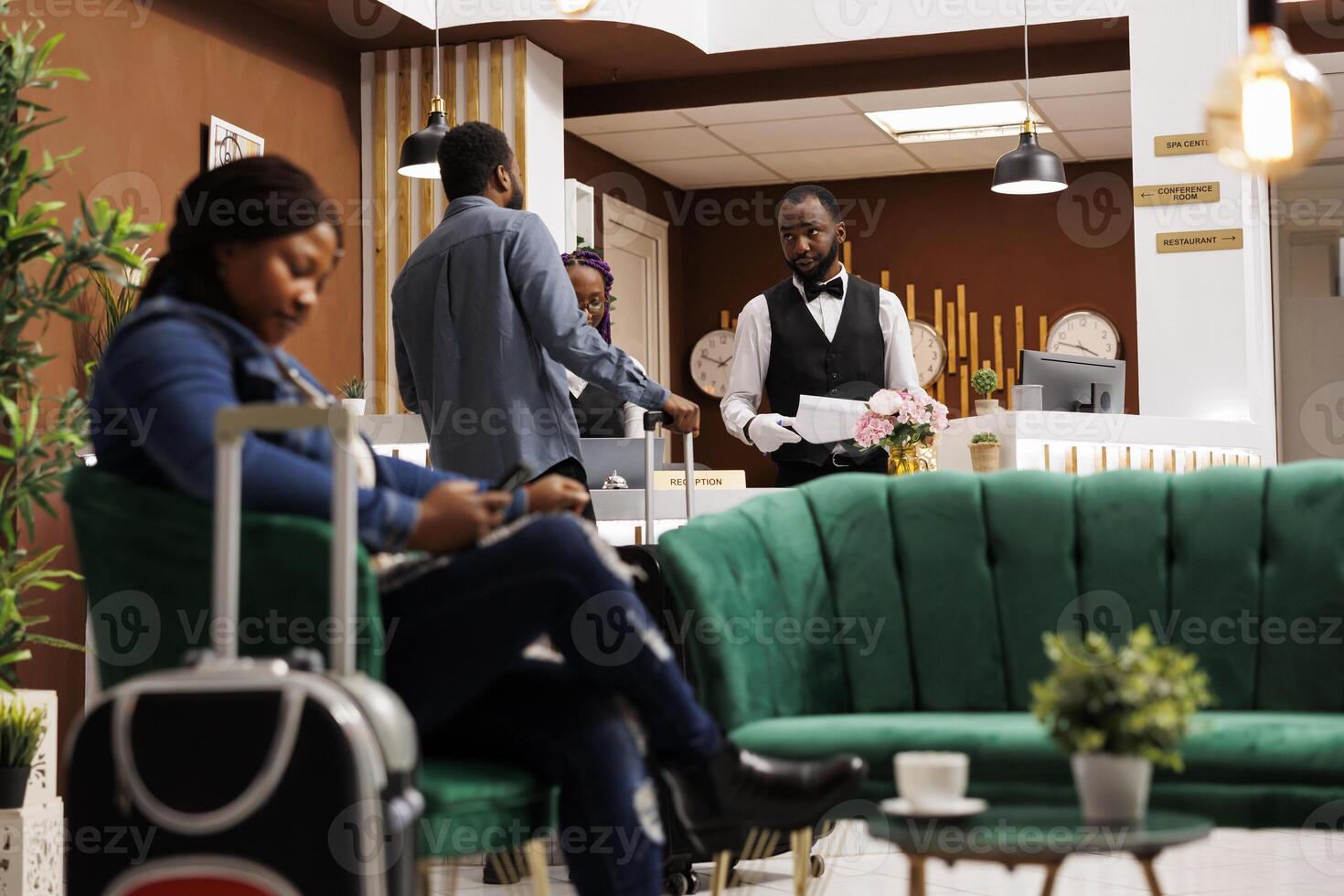 Hotel front office team welcoming and registering guest at reception desk, African American man receptionist talking with tourist completing check-in or check-out. People arriving at resort photo