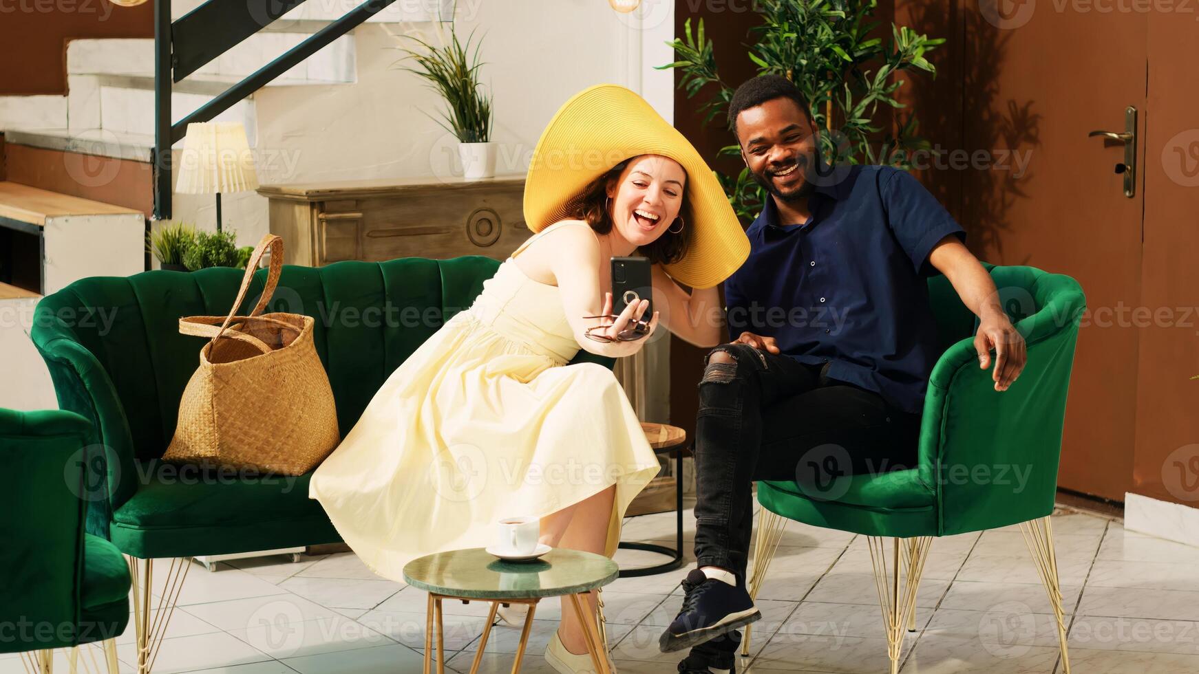 Diverse couple using videocall in hotel lobby, talking to people on online teleconference in lounge area before check in. Tourists enjoying remote video conversation at tropical seaside resort. photo