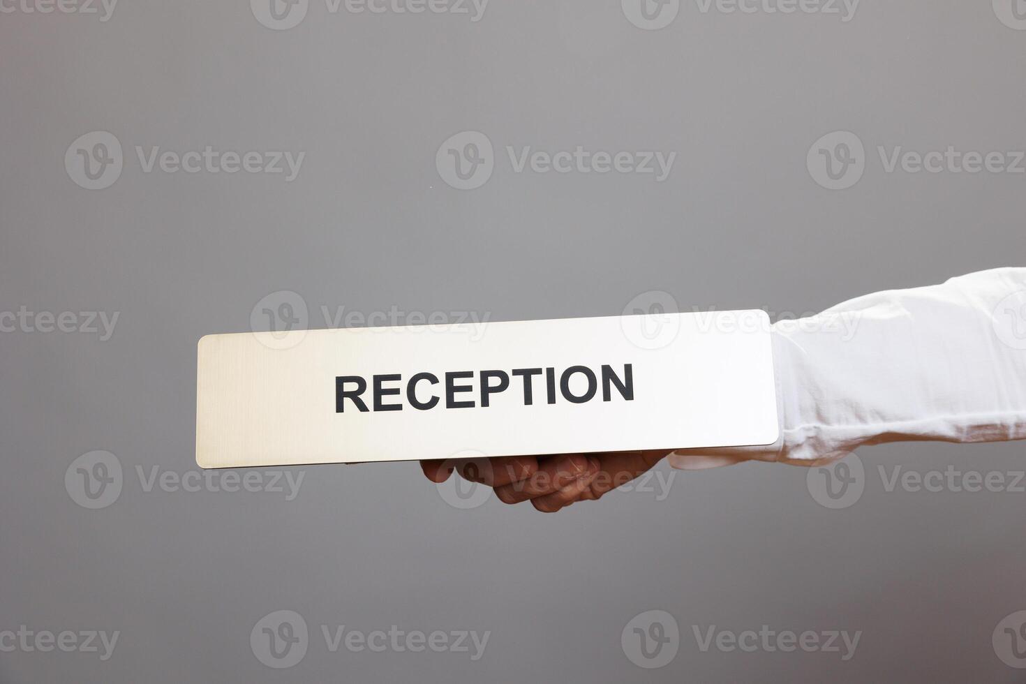 Hotel administrator hand holding reception stainless steel plate closeup. Hospitality service receptionist arm showing tabletop metal name sign close view in studio on gray background photo