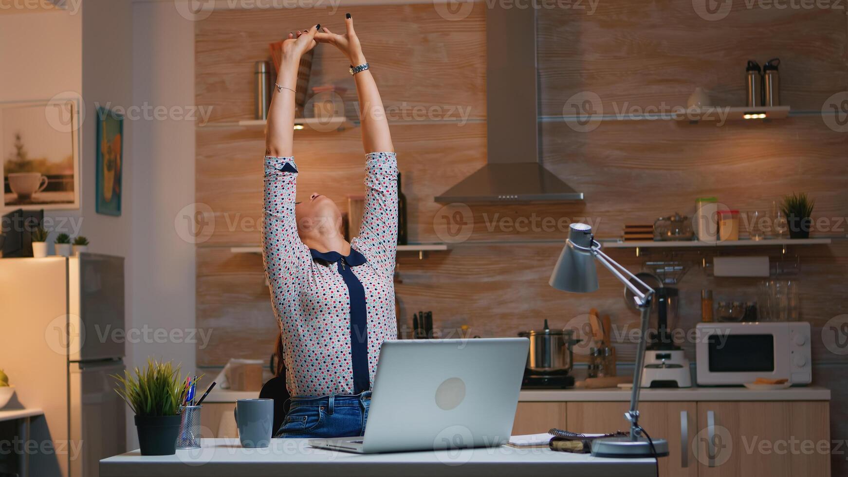 Tired woman working from home streatching after typing on laptop late at night. Busy focused employee using modern technology network wireless doing overtime for job reading writing, searching photo