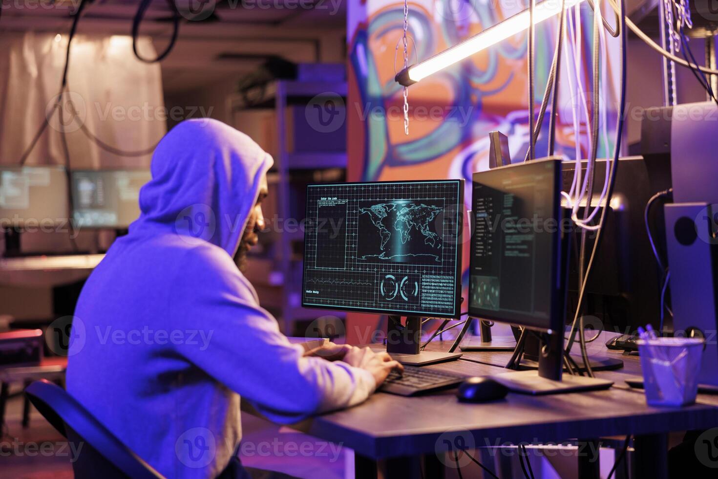 African american hacker in hood breaking into server and stealing sensitive information. Internet criminal coding malicious software for data breach on computer in dark abandoned warehouse photo