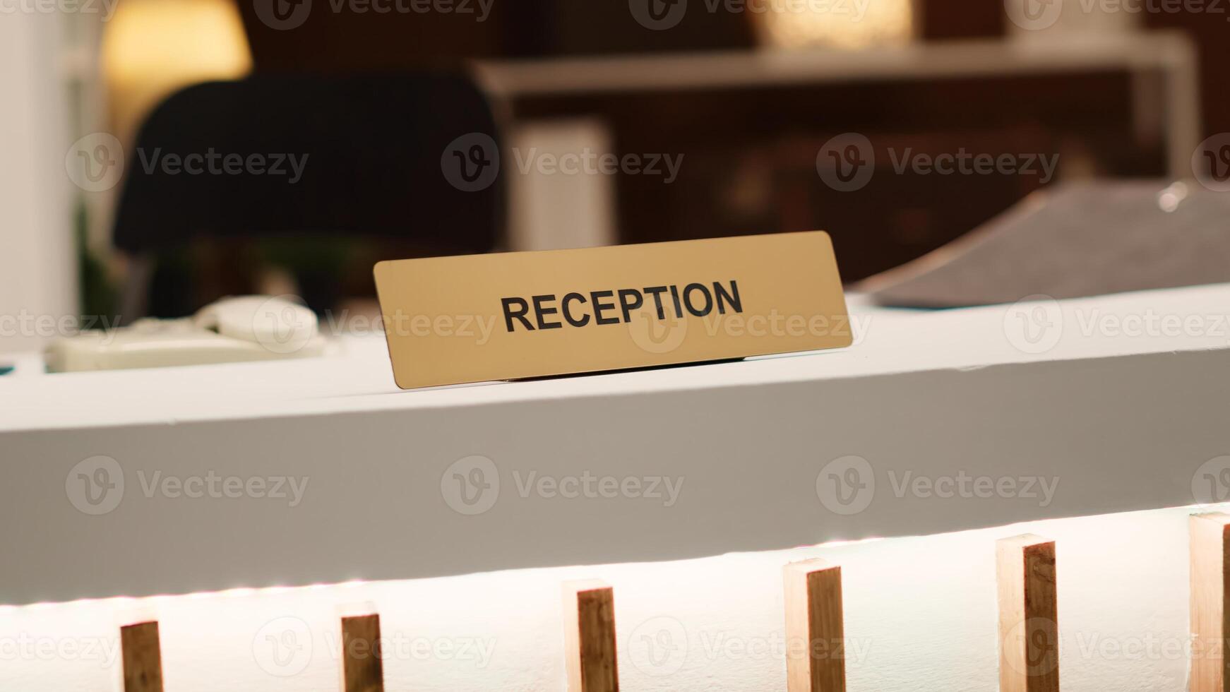 Blurry revealing extreme close up shot of reception sign on empty clean desk in stylish hotel lounge interior. Warm cozy rustic hospitality industry resort check in counter photo