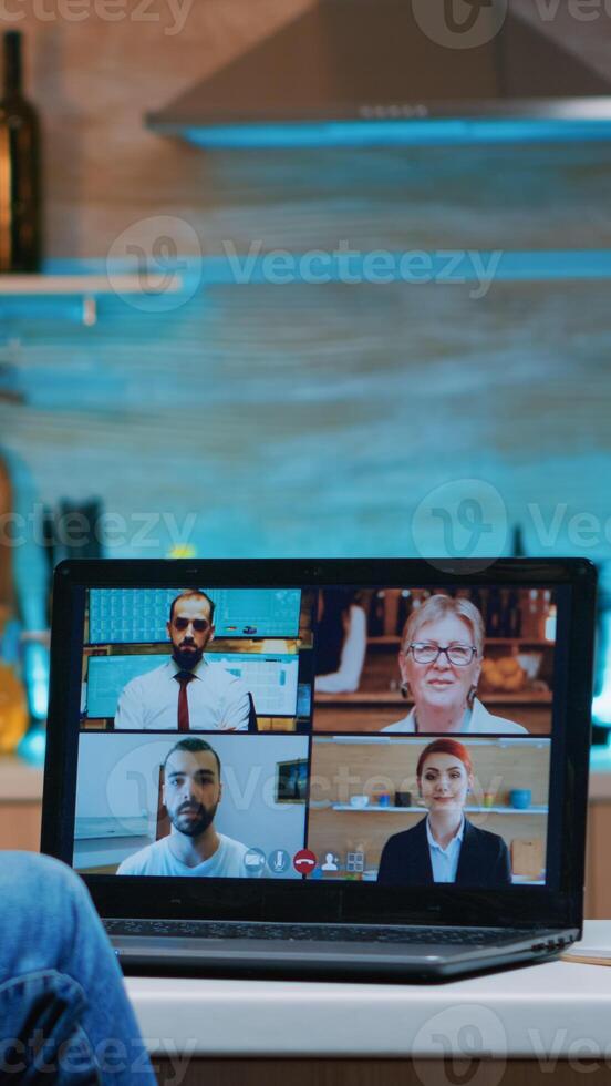 Freelancer working remotely discussing with partners online using laptop sitting in the kitchen at night. Using modern technology network wireless talking on virtual meeting at midnight doing overtime photo