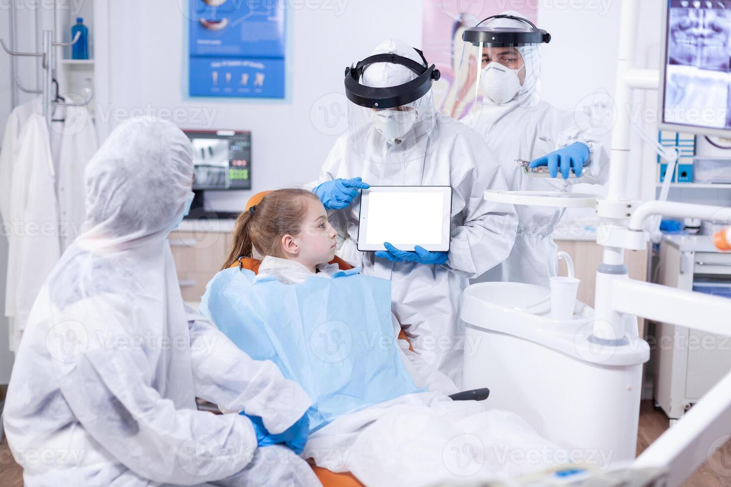 Dentist dressed in ppe suit using digital device with chroma key Medical specialist in oral hygine holding tablet pc with copy space available during global pandemic with covid19. photo
