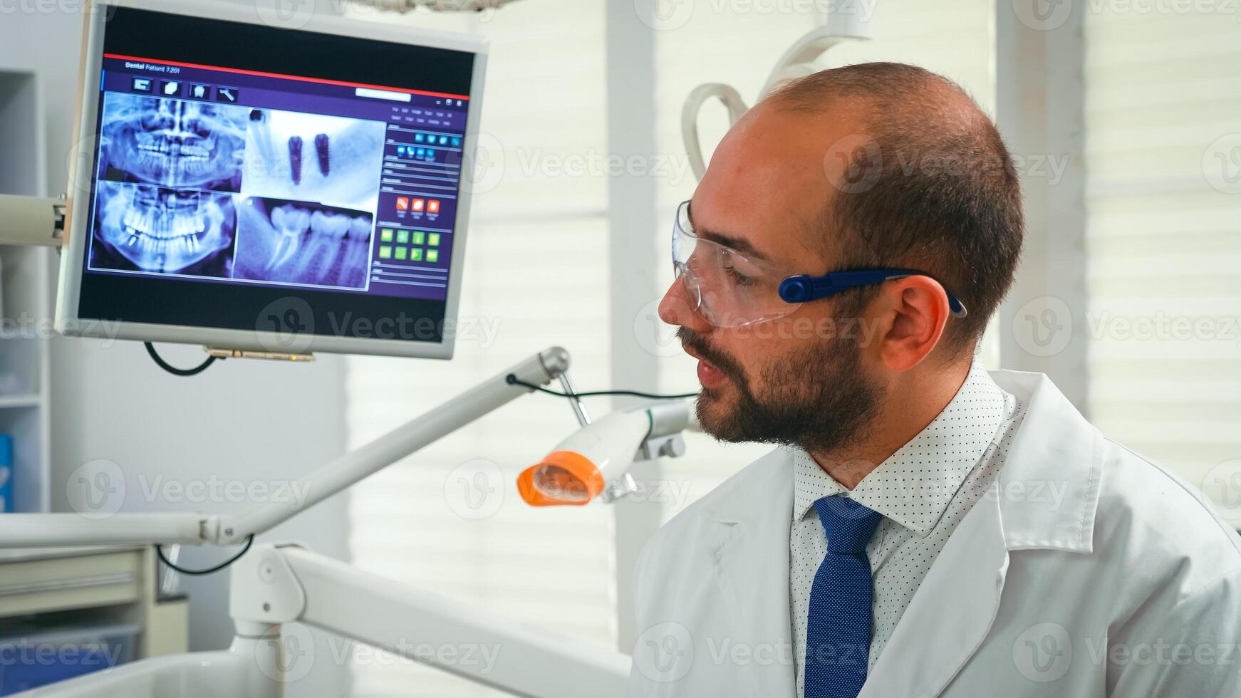 Portrait of stomatologist telling the treatment to elderly woman having digital x-ray in background. Doctor working in modern stomatological office explaining radiography of teeth from digital monitor photo
