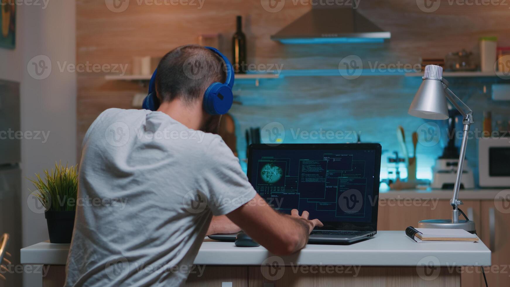 Man hacker with headset coding html and programming on screen laptop working from home in midnight. Programmer writing a dangerous malware for cyber attacks using performance device late at night photo