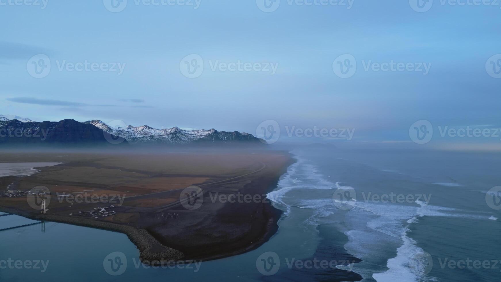 Aerial view of icelandic coastline with famous black sand beach and nordic scenery, snowy mountains and hills. Beautiful altantic ocean shore with roadside, natural panoramic view. Slow motion. photo