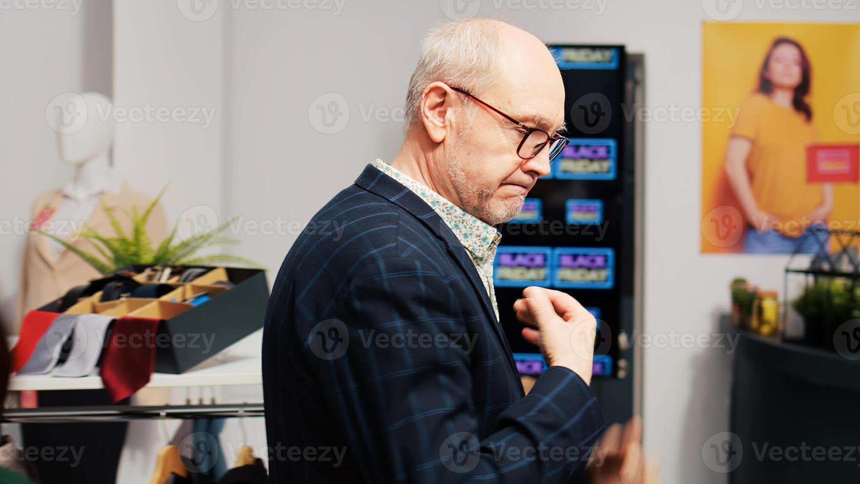 Black friday senior customer searching for discounted merchandise in clothing store during black friday sales rush. Man client checking hangers and racks with clothes, bargain hunting. photo