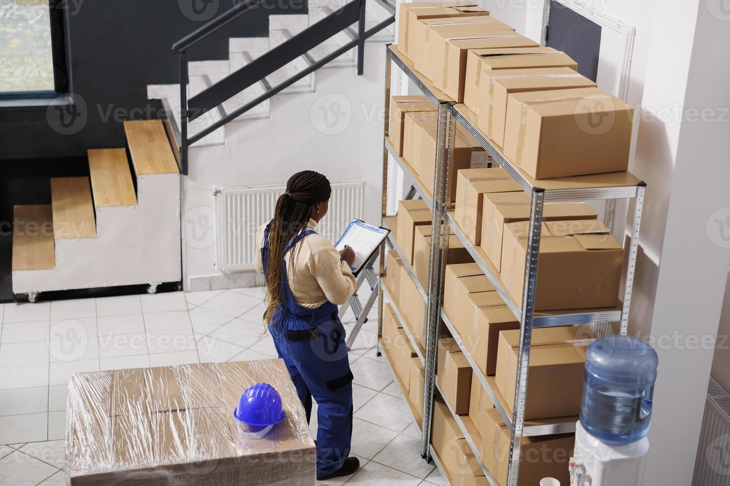 Warehouse manager checking documentation on clipboard and inspecting parcels. African american woman storehouse supervisor overseeing packages dispatching operations top view photo