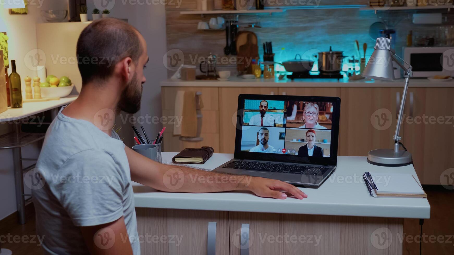 Businessman having a video conference with team during midnight using laptop in home kitchen. Corporate meeting using using modern technology network wireless talking on webcam at midnight photo