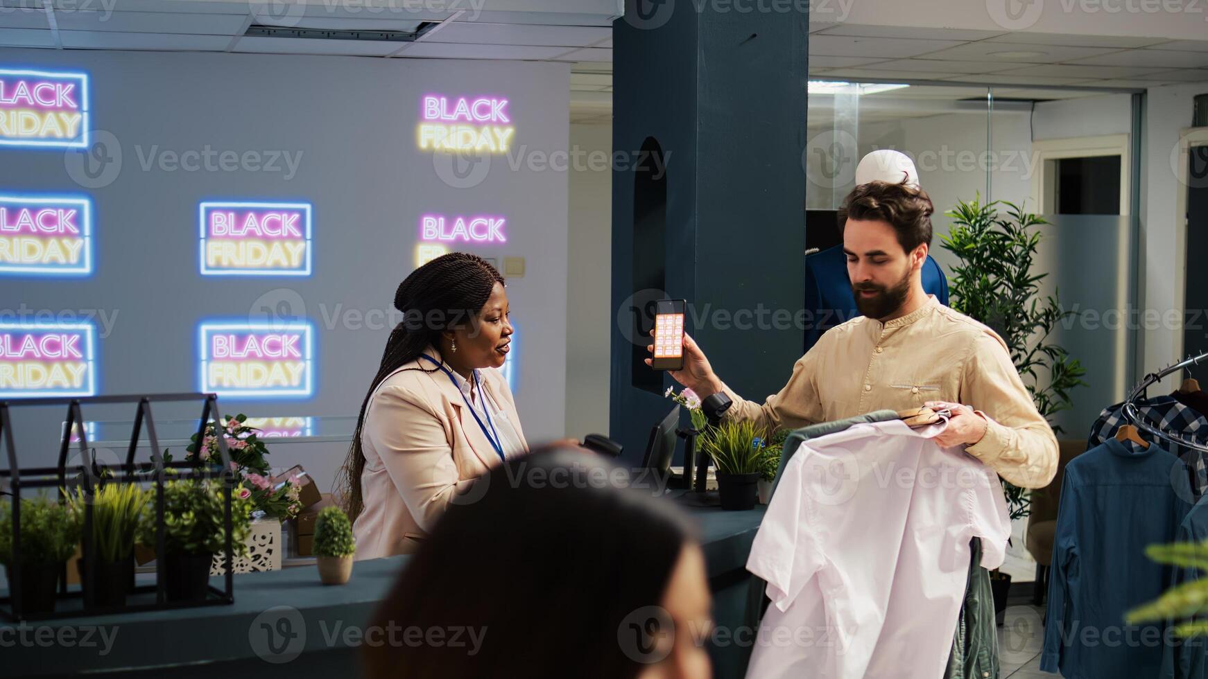 Mobile coupon marketing in retail shop. Client showing smartphone with black friday promo code to cashier, preparing to buy clothes at promotional prices. Shopper using loyalty voucher. photo