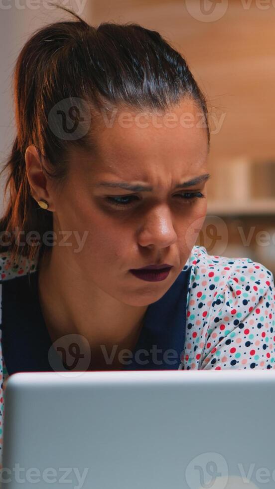 Tired freelancer squinting while reading emails working from kitchen home late at night in front of laptop. Busy focused employee using modern technology network wireless doing overtime writing, searching. photo