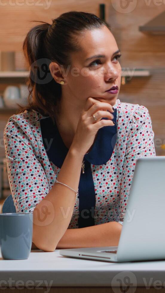 Thinking at next project while working remotly from home, reading the tasks using laptop sitting in the kitchen. Busy focused employee using modern technology network wireless doing overtime for job typing writing, searching photo