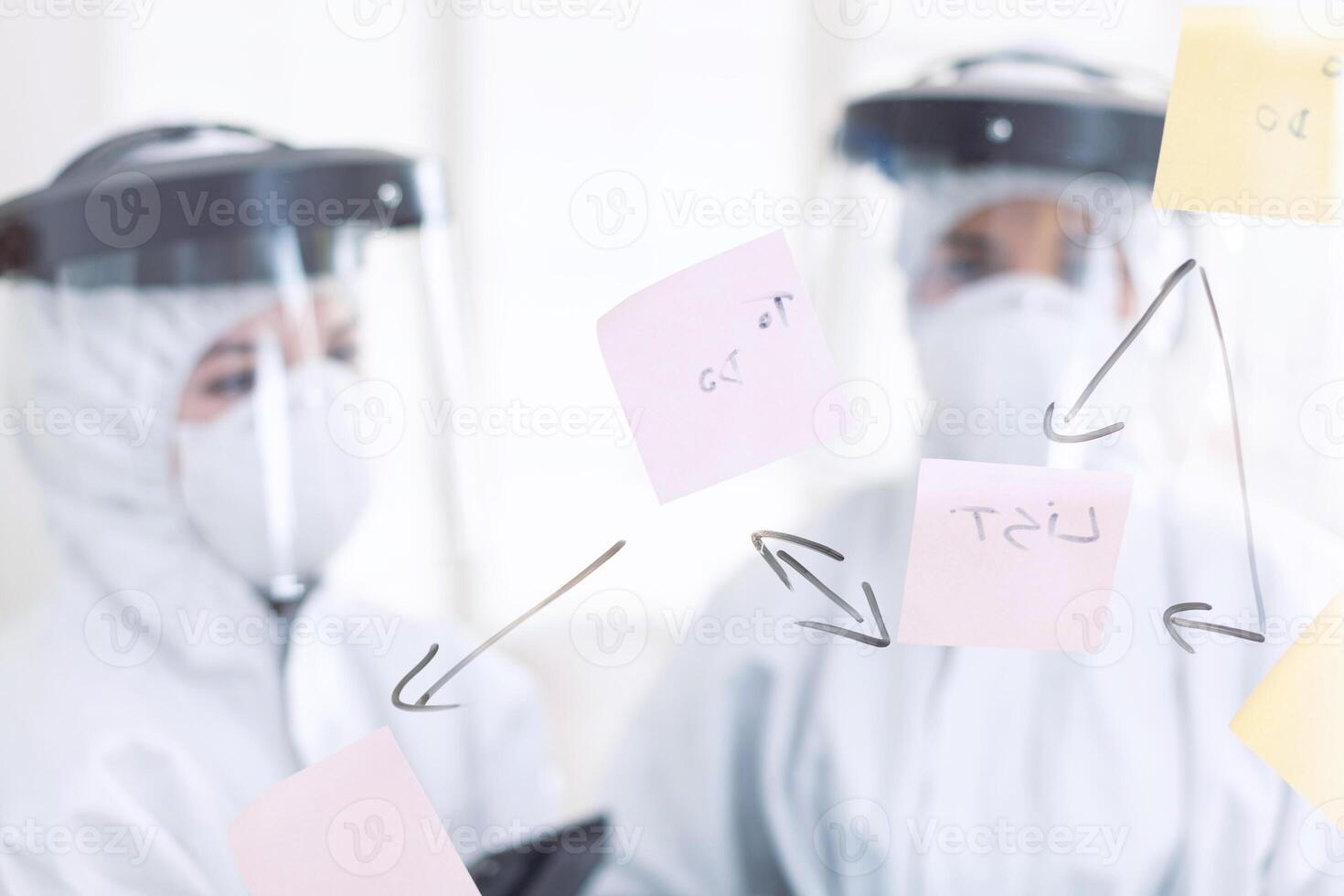 Stomatologs dressed in ppe suit during covid-19 as safety precaution. Medical team in stomatology office wearing coverall in dental office writing ideas on sticky notes. photo