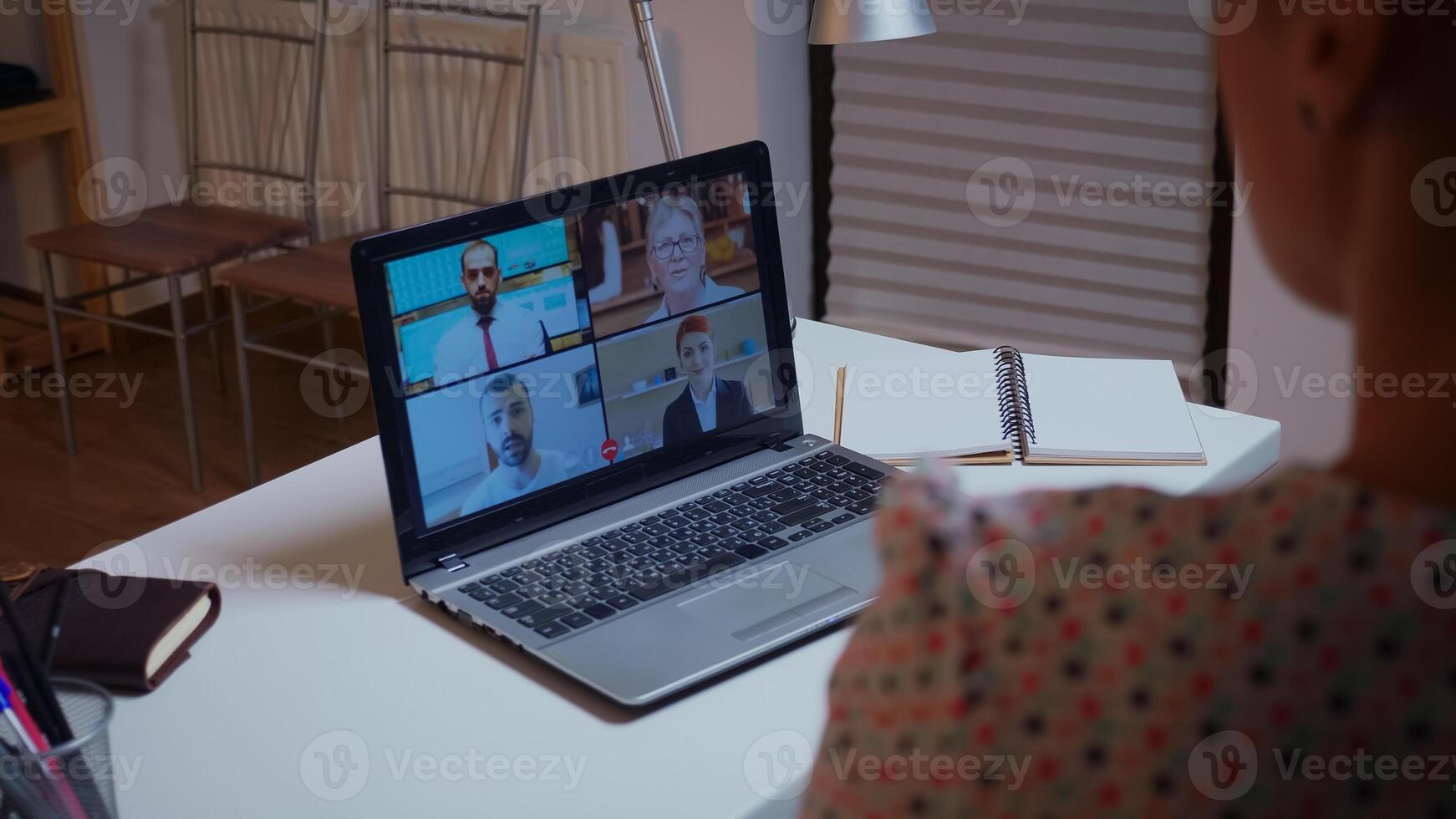 mujer de negocios teniendo un vídeo conferencia con equipo durante medianoche utilizando ordenador portátil en hogar cocina. dama utilizando moderno tecnología red inalámbrico hablando en virtual reunión a medianoche haciendo tiempo extraordinario foto