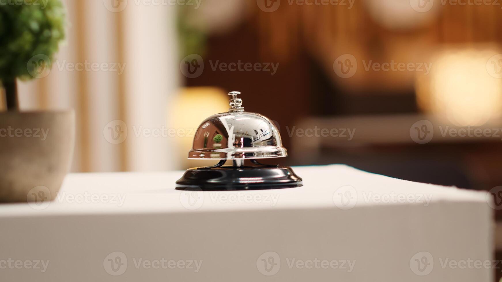 Extreme close up of concierge bell next to mini plant on cozy hotel lounge check in desk. Elegant service bell on modern stylish hospitality industry resort reception counter photo