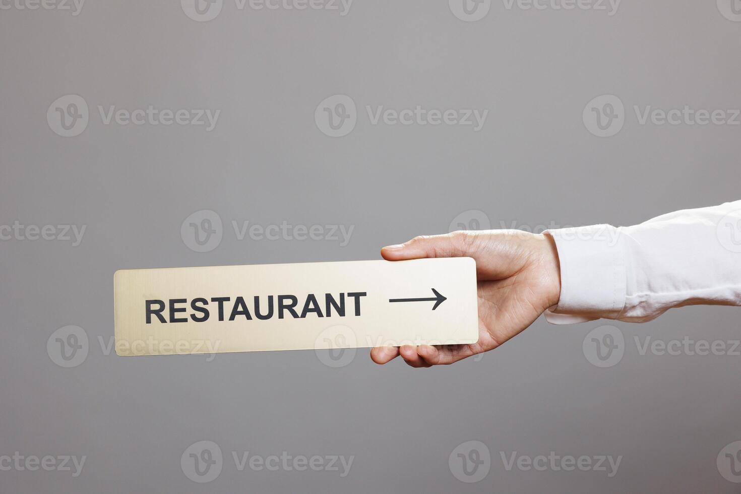 Woman hand holding restaurant directional stainless steel signage closeup. Receptionist arm showing cafeteria pointer tabletop metal sign close view in studio on gray background photo