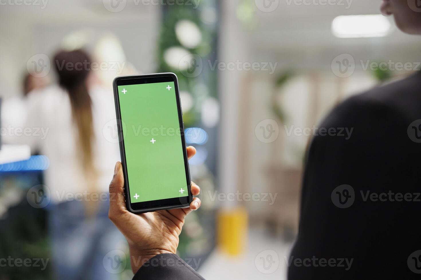 Woman holding mobile phone with green screen in hand while shopping in boutique. African american woman using smartphone with blank chroma key display in department store photo